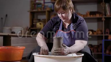 中年妇女用坐在黑暗手工作坊里的陶工轮制作陶瓷花瓶